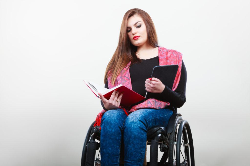Woman in wheelchair with book and tablet
