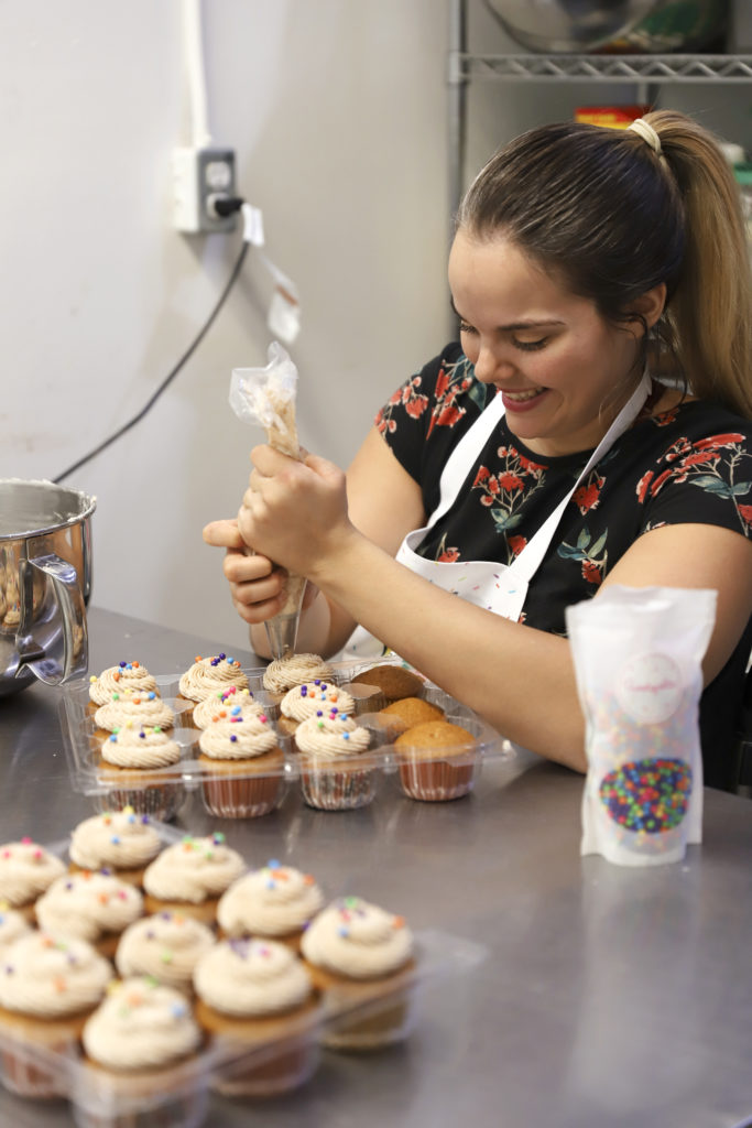 Jessica is piping icing onto cupcakes with a smile on her face
